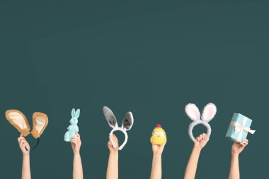 Paskalya tavşanı kulaklığı takan kadın elleri hediye kutusu, oyuncak tavuk ve koyu yeşil arka planda tavşan