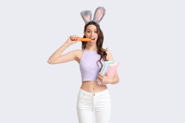 Paskalya tavşanı kulaklıklı, beyaz arka planda havuç yiyen genç bir kadın.