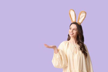Paskalya tavşanı kulaklıklı mutlu genç kadın eflatun arka plandaki bir şeyi işaret ediyor.