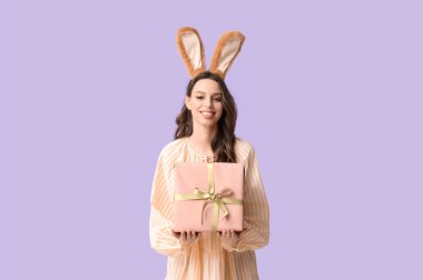 Paskalya tavşanı kulaklıklı mutlu genç kadın. Leylak arkaplanda hediye paketi var.