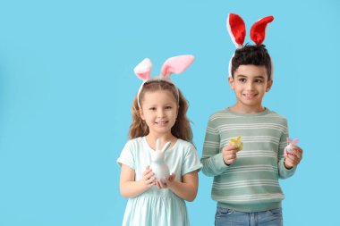 Tavşan kulaklı şirin çocuklar ve mavi arka planda Paskalya yumurtaları.