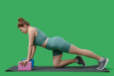 Spor yapan genç bir kadın yeşil arka planda egzersiz yapıyor.