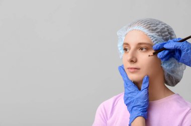 Plastik cerrah, gri arka planda kadın yüzüne izler uyguluyor. Blepharoplasty konsepti