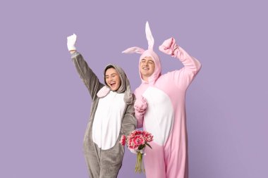 Mor arka planda bir buket lale olan tavşan kostümlü güzel bir çift. Paskalya kutlaması