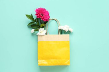 Turkuaz arka planda çiçekli kağıt alışveriş torbası.