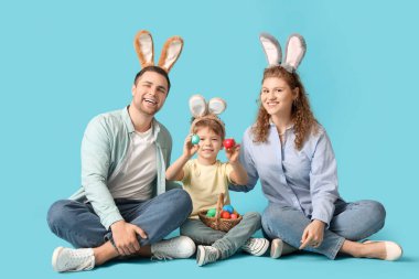 Aile mavi arka planda boyalı Paskalya yumurtalarıyla oturuyor.