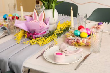 Çiçekler, mumlar ve boyalı yumurtalarla dolu güzel bir Paskalya masası.