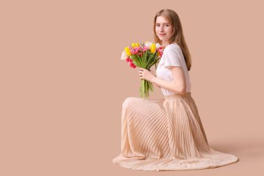 Kahverengi arka planda bir buket lale olan güzel genç bir kadın.