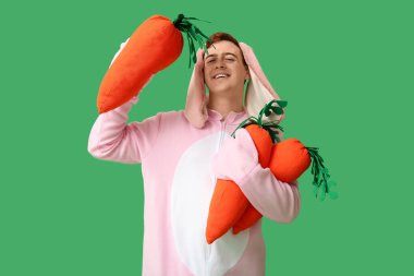 Paskalya tavşanı kostümlü mutlu genç adam yeşil arka planda peluş havuçlar