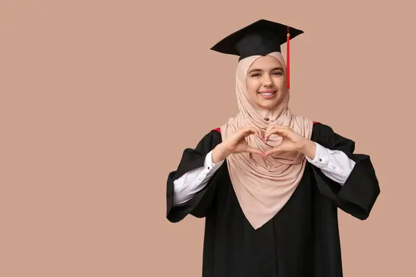 행복한 무슬림 졸업생 베이지 배경에 그녀의 손으로 마음을 만드는 — 스톡 사진