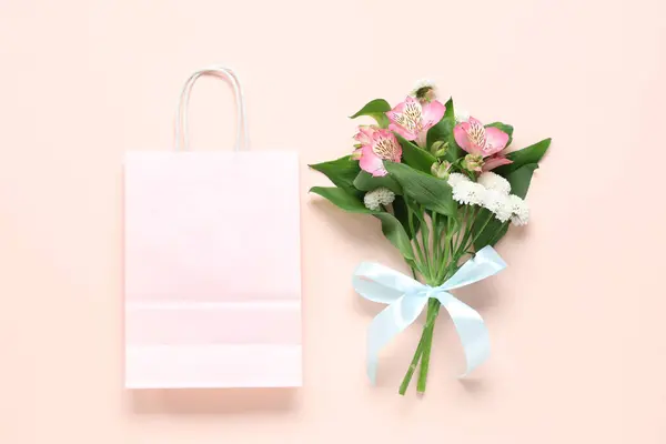 Paper shopping bag with flowers and ribbon on beige background