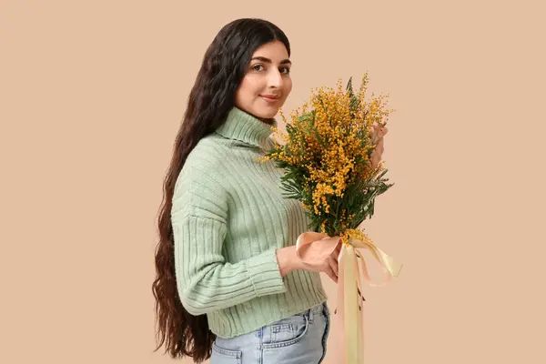 Beautiful young woman with bouquet of mimosa flowers on beige background