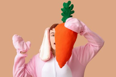 Paskalya tavşanı kostümlü, bej arka planda peluş havuçlu genç adam.