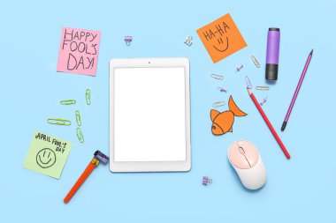 Modern tablet, ataç ve mavi arka planda yapışkan notlar. 1 Nisan şakası.
