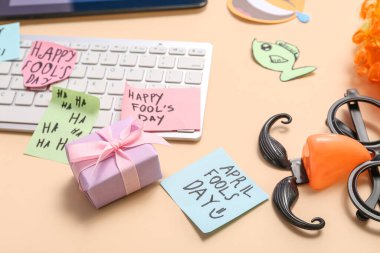 Bilgisayar klavyesi, hediye kutusu, palyaço kostümü ve bej arka planda yapışkan notalar. 1 Nisan şakası.