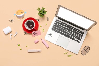 Laptop, bir fincan kahve ve bej arka planda yapışkan notlar. 1 Nisan şakası.