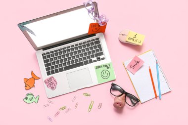 Laptop, dizüstü bilgisayar ve pembe arka plandaki yapışkan notlar. 1 Nisan şakası.