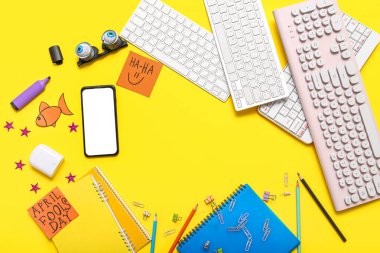 Telefondan yapılmış çerçeve, bilgisayar klavyeleri, not defterleri ve sarı arkaplandaki yapışkan notlar. 1 Nisan şakası.