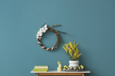 Tavşanlı masa, mimoza çiçekleri vazosu ve duvarda geleneksel Paskalya çelengi.