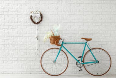 Beyaz tuğla duvarda geleneksel Paskalya çelengi ve çiçek dolu bisiklet.