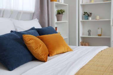 Rahat yatak, raf ünitesi, ev bitkileri ve yastıklar modern yatak odasında.