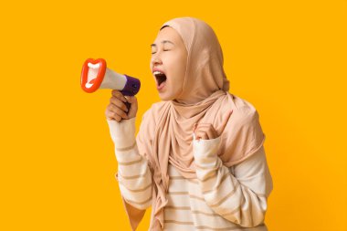 Genç Asyalı Müslüman kadın sarı arka planda komik megafona bağırıyor. Ulusal Duyulma Günü