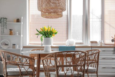 Yemek masası ve vazoda sarı laleler olan şık bir mutfak.