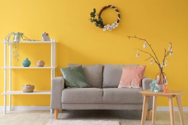 İçinde ağaç dalları ve Paskalya yumurtaları olan bir vazo şık oturma odasının içinde.