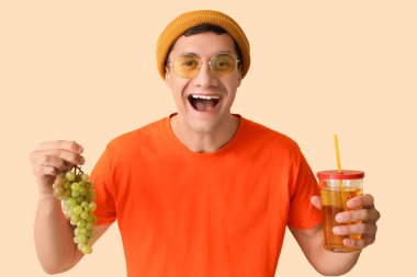 Bej arka planda üzüm ve bir bardak meyve suyu olan mutlu genç adam.