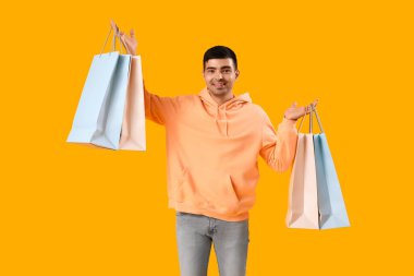 Sarı arka planda alışveriş torbaları olan yakışıklı bir genç.
