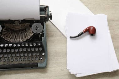 Sigara piposu ve bej ahşap masa üzerinde kağıt çarşaflı klasik daktilo.