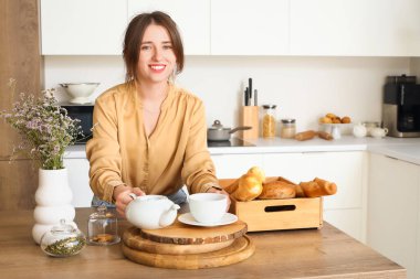 Young woman with teapot at table in kitchen