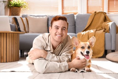 Evde yerde yatan sevimli Corgi köpeği olan kızıl saçlı mutlu genç adam.