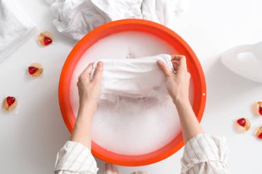 Çamaşırları leğende, beyaz masada suyla yıkayan bir kadın.