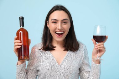 Mavi arka planda cam ve kırmızı şarap şişesi olan güzel genç bir kadın.