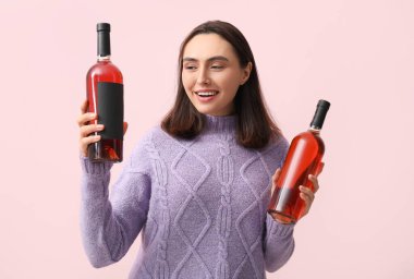 Pembe arka planda kırmızı şarap şişeleri olan güzel genç bir kadın.