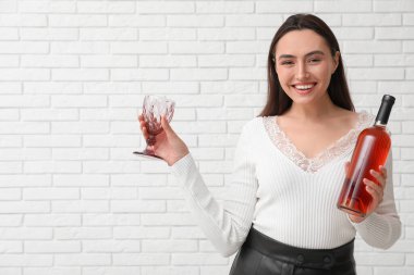 Beyaz tuğlalı arka planda cam ve şarap şişesi olan güzel genç bir kadın.