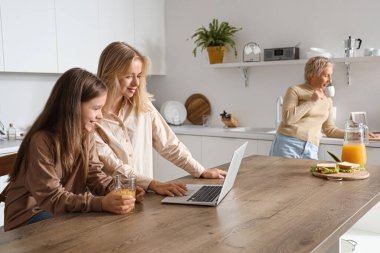 Annesiyle küçük kız mutfakta dizüstü bilgisayar kullanıyor.