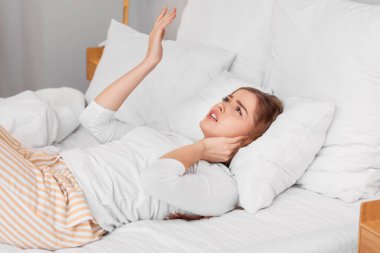 Young woman with pillow suffering from loud neighbours in bedroom clipart