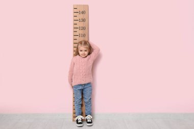 Pembe duvarın yanında boyunu ölçen sevimli küçük bir kız.