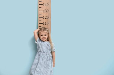 Mavi arka planda boyunu ölçen tatlı küçük bir kız.