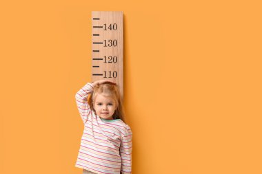 Sarı arka planda boyunu ölçen tatlı küçük bir kız.