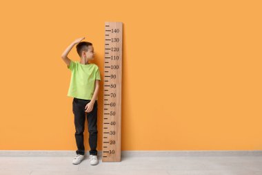 Sarı duvarın yanında boyunu ölçen sevimli küçük bir çocuk.