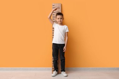 Sarı duvarın yanında boyunu ölçen sevimli küçük bir çocuk.