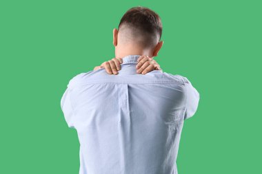 Yeşil arka planda sırt ağrısı çeken genç bir adam.