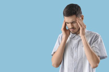 Mavi arka planda migren ağrısı çeken genç bir adam.