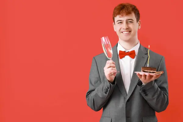 Young man with piece of birthday cake and champagne on red background
