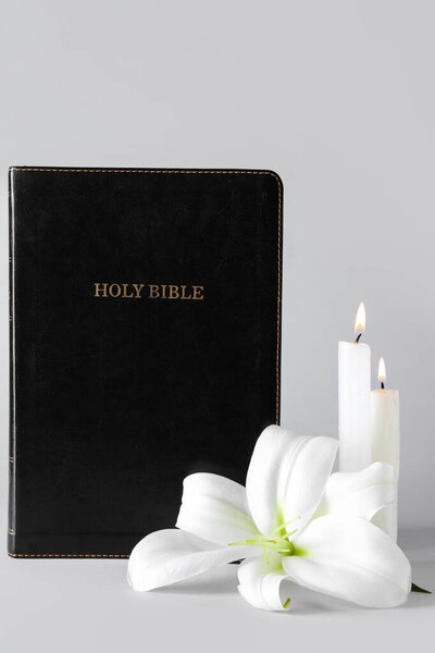 Beautiful lily flower, burning candles and Holy Bible on grey background