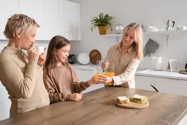 Little girl with her mom and grandmother having breakfast in kitchen