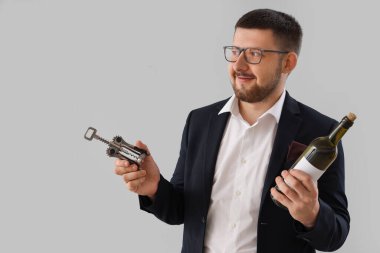 Gri arka planda şarap şişesi ve açacağı olan genç şarap garsonu.